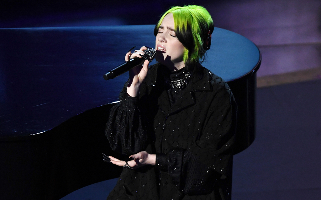 Billie Eilish wore a custom Gucci black crystal GG embroidered oversized short sleeve bowling shirt with a black crystal embroidered turtleneck, black crystal GG embroidered pants and black leather Flashtrek sneakers with spikes. She completed her look with a pair of sterling silver GG earrings, lion head choker in metal with aged palladium finish, GG ring in metal with aged palladium finish and crystals, lion head ring in aged palladium finish and a GG hair barrette in black and red resin. 